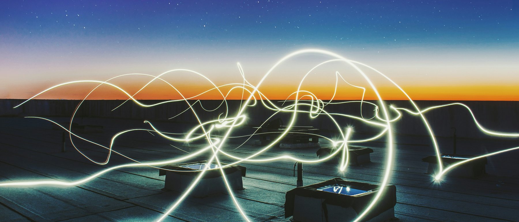 Long-exposure light trails tracing across a rooftop at dusk